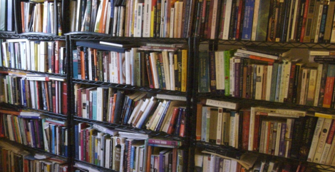 A wall covered in shelves all stuffed full of books. Light shines on the left-side of the image.